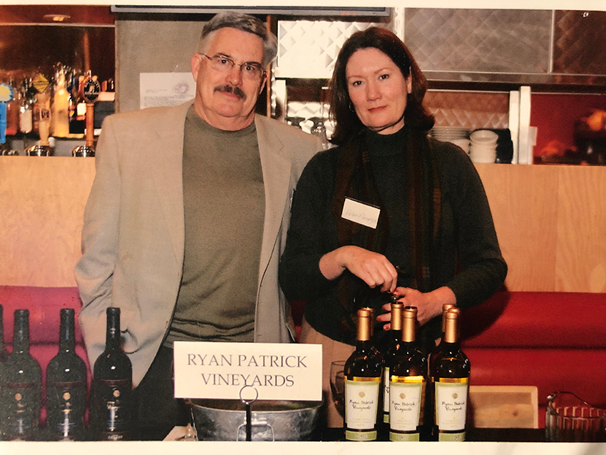 Man and woman standing in front of table with wine glasses and bottles at a tasting event